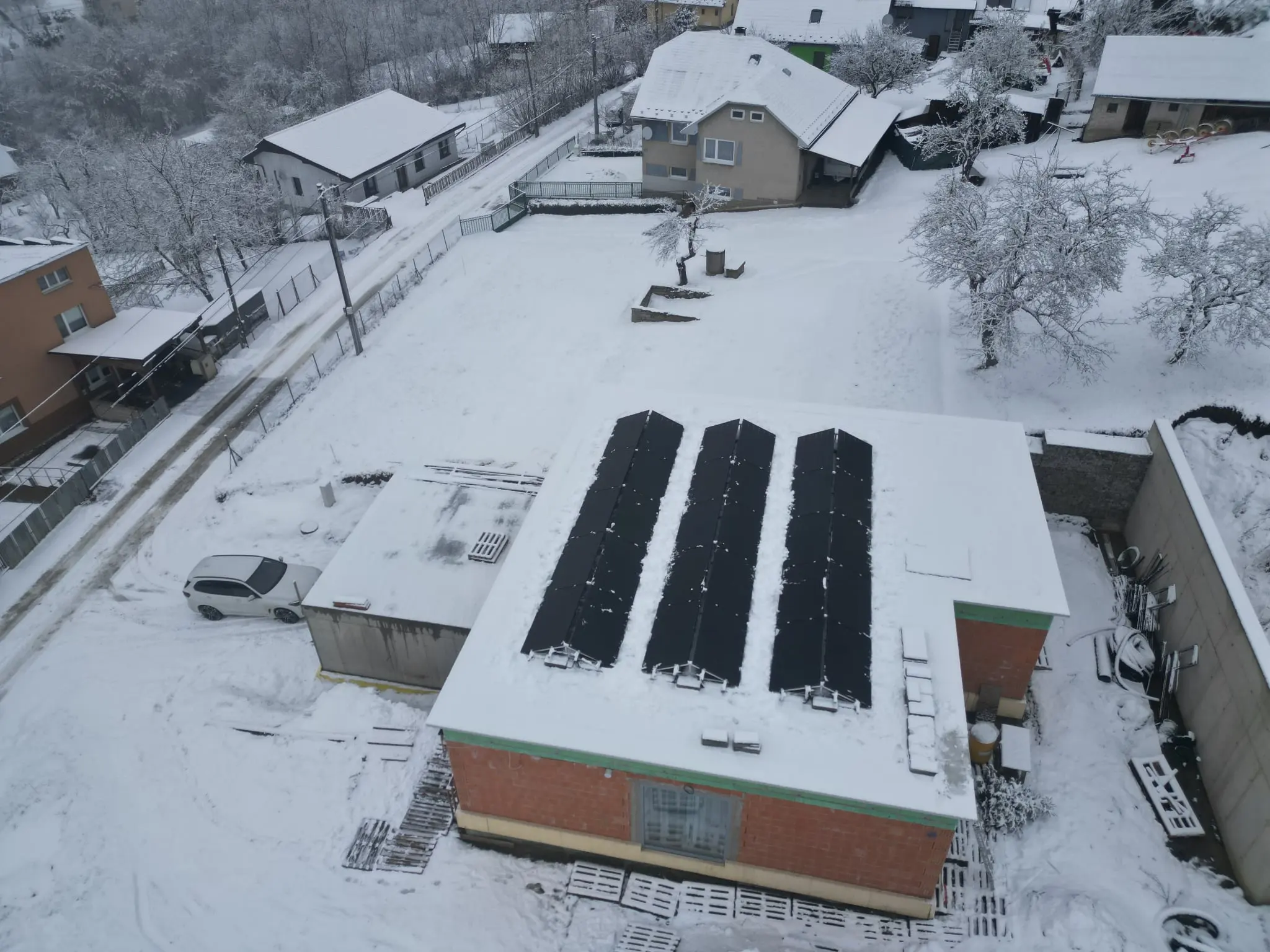 Zimný záber z dronu na strechu haly s tromi radmi fotovoltických panelov.